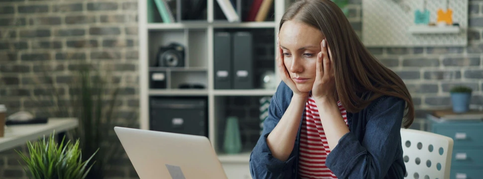 Eine Frau sitzt am Computer und hält sich die Hände über den Kopf