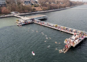 Steg auf dem Wasser ist gefüllt mit Menschen. Im Wasser sieht man auch Menschen schwimmen. Das Bild ist von oben gemacht wurden