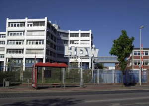 HDW-Verwaltungsgebäude in Kiel bei sonnigem Wetter. Verwaltungsgebäude der HDW in Kiel mit großem HDW-Schriftzug und Bushaltestelle im Vordergrund.
