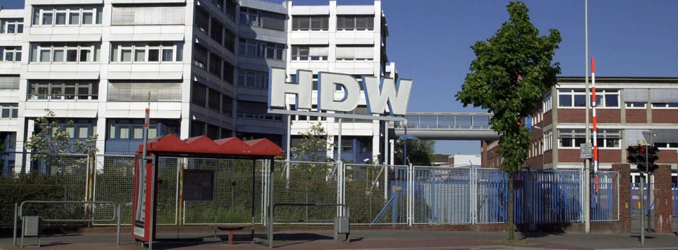 Verwaltungsgebäude der HDW in Kiel mit großem HDW-Schriftzug und Bushaltestelle im Vordergrund.