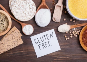 Glutenfreie Zutatenvielfalt für bewusste Ernährung. Verschiedene glutenfreie Lebensmittel wie Reis, Mehl, Mais und Knäckebrot auf Holztisch mit „Gluten Free“-Hinweis.
