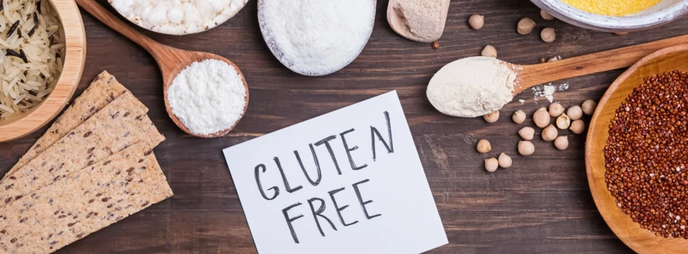 Glutenfreie Zutatenvielfalt für bewusste Ernährung. Verschiedene glutenfreie Lebensmittel wie Reis, Mehl, Mais und Knäckebrot auf Holztisch mit „Gluten Free“-Hinweis.