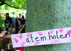 Beim Flohmarkt in der Alten Mu gibt es allerlei Schätze zu entdecken Baum mit einem Schild, im Hintergrund Menschen an einem Tisch