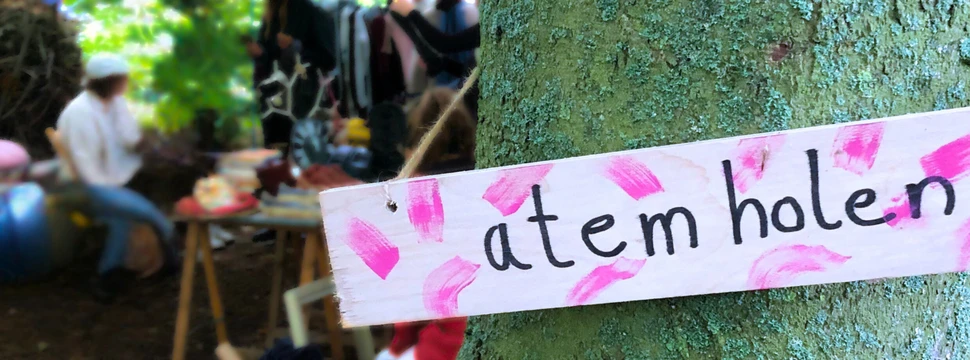Beim Flohmarkt in der Alten Mu gibt es allerlei Schätze zu entdecken Baum mit einem Schild, im Hintergrund Menschen an einem Tisch