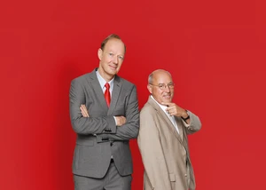 Gregor Gysi und Martin Sonneborn stehen nebeneinander vor einem rotem Hintergrund