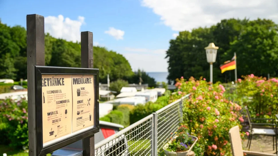 Ein Campingplatz mit grünen Hecken und Bäumen sowie einer Speise- und Getränkekartentafel am Meer