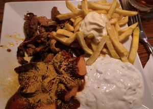 Ein Teller, auf dem Currywurst, Pommes und Tzaziki gemeinsam mit Gyros angerichtet sind