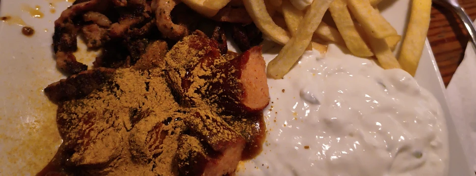 Ein Teller, auf dem Currywurst, Pommes und Tzaziki gemeinsam mit Gyros angerichtet sind