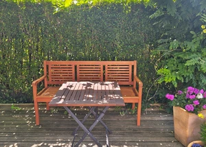 Eine Sitzbank in einem Garten mit einer Hecke im Hintergrund