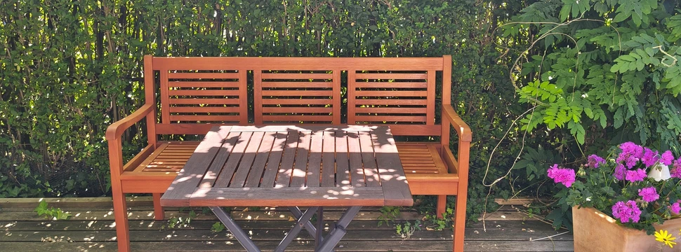 Eine Sitzbank in einem Garten mit einer Hecke im Hintergrund