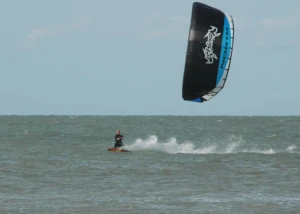 Kitesurfer in voller Fahrt auf dem Meer. Kitesurfer fährt über wellige See mit großem schwarzen und blauen Kite.