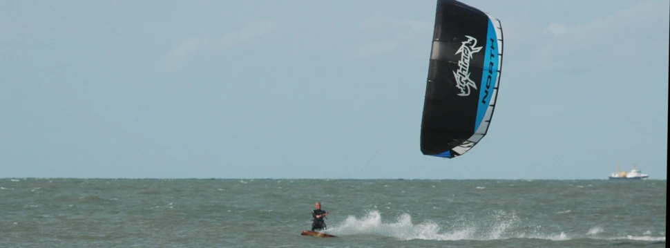 Kitesurfer in voller Fahrt auf dem Meer. Kitesurfer fährt über wellige See mit großem schwarzen und blauen Kite.