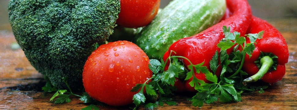 Frisches Gemüse mit Brokkoli, Tomaten, Gurke, Paprika und Petersilie auf Holzunterlage.