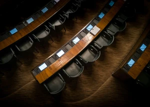 Schwarze Stühle stehen nebeneinander vor einem langem Holztisch