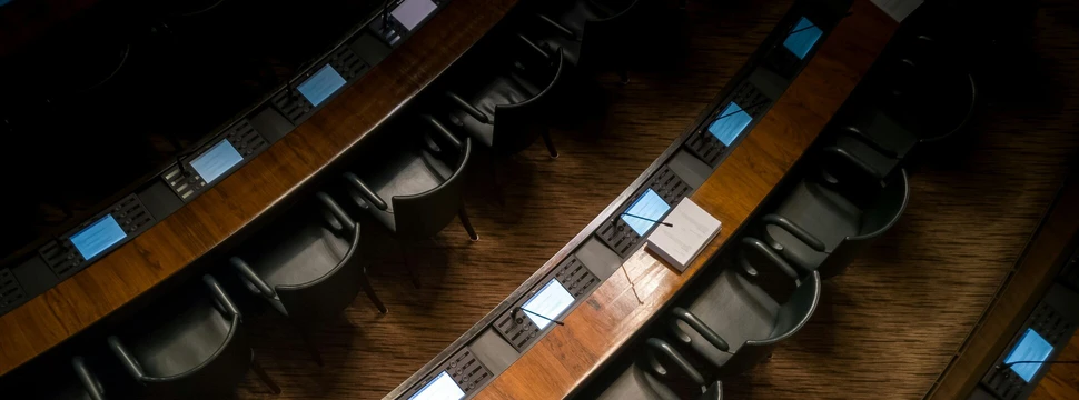 Schwarze Stühle stehen nebeneinander vor einem langem Holztisch