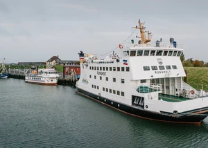 Fähren im Hafen von Pellworm Schiffe mit den Namen "Rungholt" und "Nordfriesland" in einem Hafen mit Gebäuden und dem Deich im Hintergrund