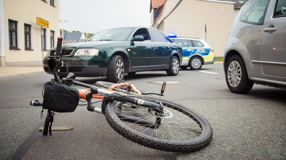 Umgestürztes Fahrrad auf Asphalt mit Polizeiauto im Hintergrund nach Verkehrsunfall in Wohngebiet