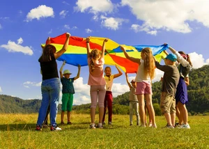 Kinder mit bunten Schwingtuch. Sie stehen im Kreis und heben das Tuch hoch