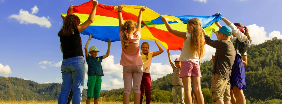 Kinder mit bunten Schwingtuch. Sie stehen im Kreis und heben das Tuch hoch