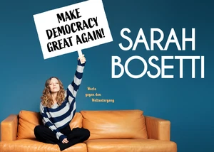 Frau sitzt auf einem Sofa und hält ein Schild hoch mit der Aufschrift: Make democracy great again