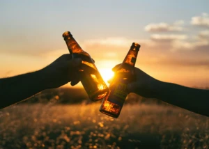 Am Vatertag könnt ihr eine schöne Zeit mit euren Vätern verbringen Zwei Bierflaschen werden aneinandergestoßen, im Hintergrund Sonnenuntergang