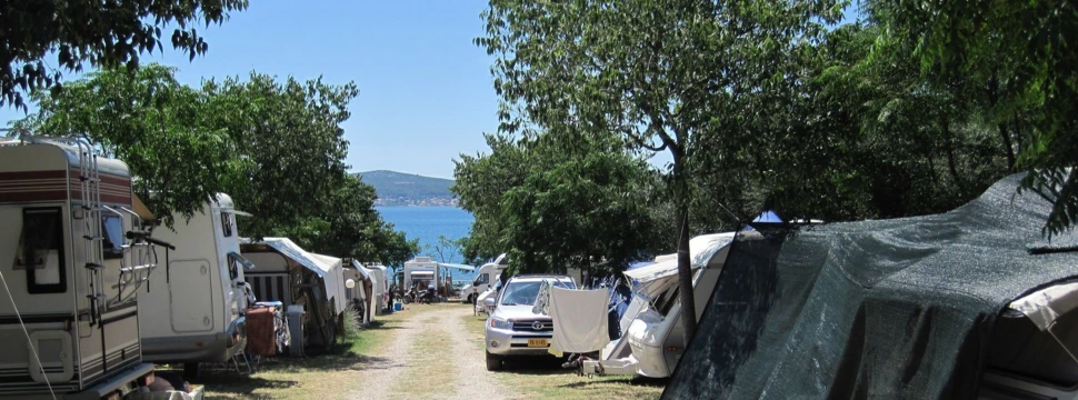 Campingplatz mit Bäumen am Meer vor blauem Himmel