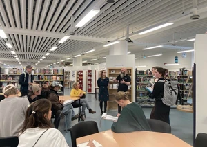 Mehrere Menschen in einem Raum mit Deckenlampen und Regalen im Hintergrund, die sich beraten und austauschen