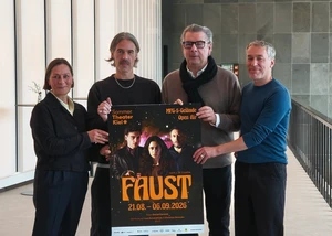 Vier Menschen mit einem Plakat in der Hand, auf dem das Theaterstück "Faust" vorgestellt wird, das im Sommer auf dem MFG-5 Gelände in Holtenau aufgeführt wird