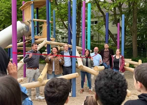 Foto der Eröffnung des neuen Schulhofs, bei der mehrere Menschen vor einem Band stehen, das den Schulhof durch Zerschneiden eingeweiht hat