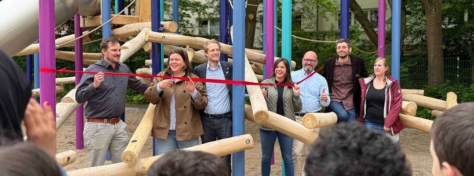 Foto der Eröffnung des neuen Schulhofs, bei der mehrere Menschen vor einem Band stehen, das den Schulhof durch Zerschneiden eingeweiht hat