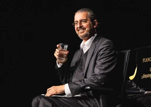 Hagen Rether sitzt und hält ein Glas Wasser in der Hand