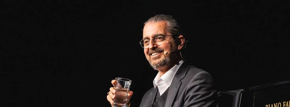 Hagen Rether sitzt und hält ein Glas Wasser in der Hand