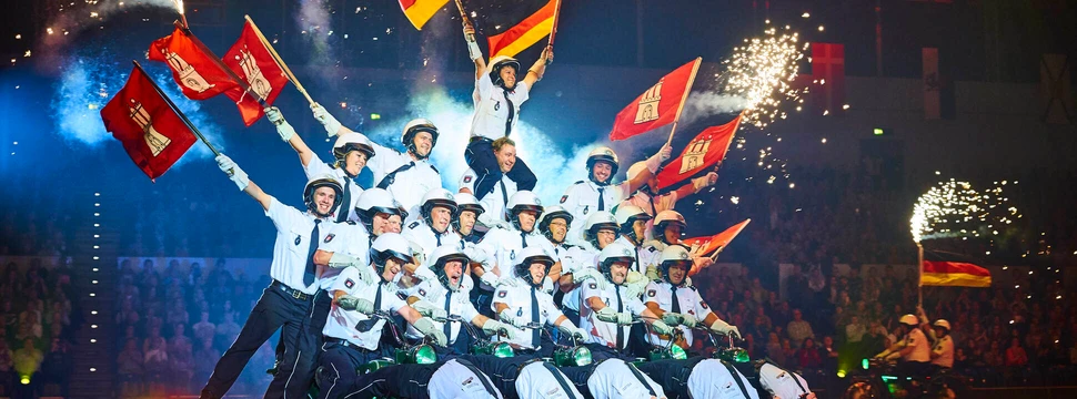 Mehrere Menschen in Polizeiuniform auf einer Bühne mit Hamburg-Flaggen in den Händen auf Motorrädern, hinter denen Funken aufflammen
