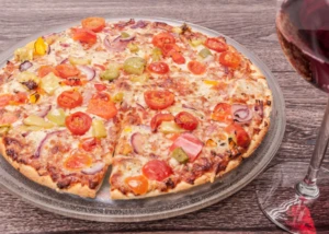 Vegetarische Pizza mit Rotwein als Begleitung Gemüse-Pizza mit Tomaten, Paprika und Zwiebeln auf Glasplatte neben einem Glas Rotwein