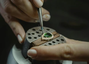 Ein Schmuckstück auf einer Presse, an dem mit einer Pinzette gearbeitet wird