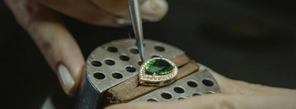 Ein Schmuckstück auf einer Presse, an dem mit einer Pinzette gearbeitet wird