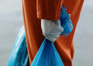 Ein blauer Müllsack in der Hand eines Menschens, der einen weißen Handschuh und eine orangene Hose trägt