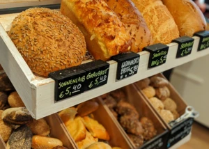 Auswahl an frischen Broten und Brötchen in der Auslage einer Bäckerei. Verschiedene Brote und Brötchen in einer Bäckertheke mit handbeschrifteten Preisschildern.