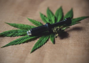 Cannabisblatt mit CBD-Öl und Blüte auf Naturstoff. Cannabisblatt mit Blüte und schwarzer Dosierspritze voller Öl auf Leinentuch.
