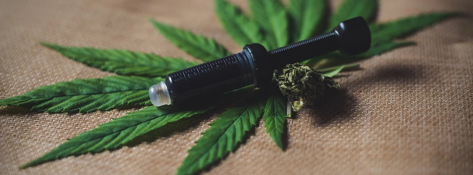 Cannabisblatt mit Blüte und schwarzer Dosierspritze voller Öl auf Leinentuch.