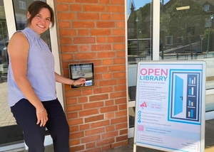 Eine Frau in einem hellen Oberteil vor der Tür der Stadtteilbücherei Pries/Friedrichsort, die ab sofort als sogenannte "Open Library" fungiert
