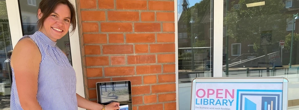 Eine Frau in einem hellen Oberteil vor der Tür der Stadtteilbücherei Pries/Friedrichsort, die ab sofort als sogenannte "Open Library" fungiert