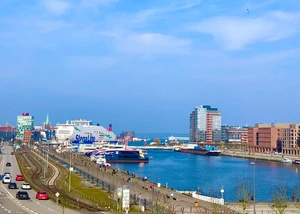 Ein lebendiger Stadthafen mit Fähren und moderner Architektur bei strahlendem Sonnenschein. Hafenpanorama mit Stena Line-Fähre, modernen Gebäuden und Promenade bei blauem Himmel.