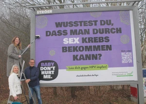 Drei Menschen vor einem frisch aufgetragenen Plakat, auf dem auf eine Kampagne hingewiesen wird, die sich für Krebsvorsorge einsetzt