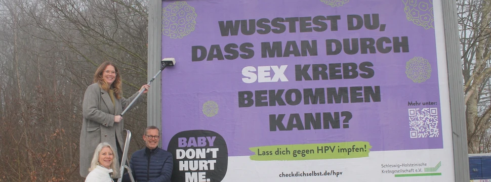 Drei Menschen vor einem frisch aufgetragenen Plakat, auf dem auf eine Kampagne hingewiesen wird, die sich für Krebsvorsorge einsetzt