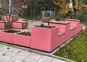 Pinke Sitzmöglichkeiten mit Grünpflanzen dazwischen vor einem Gebäude