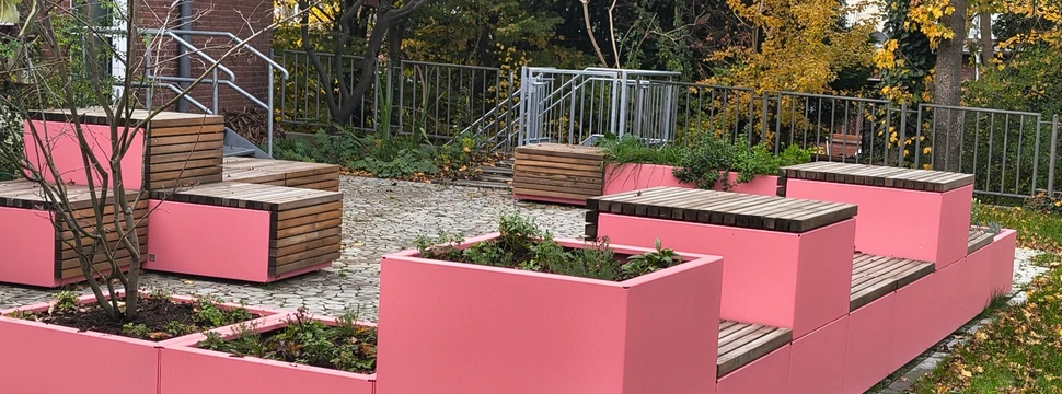 Pinke Sitzmöglichkeiten mit Grünpflanzen dazwischen vor einem Gebäude