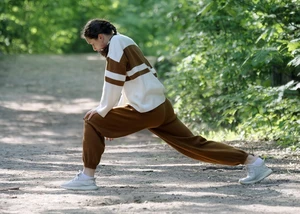 Eine Frau in braun-weißer Sportkleidung, die sich vor grünen Pflanzen am Dehnen ist