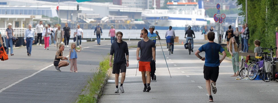 Auf einer Straße sind viele Menschen zu sehen die verschiedene Dinge tun: Laufen, Fahrradfahren, sparzieren