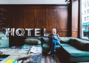 Entspannter Moment in einer stilvollen Hotellobby mit Blick auf die Stadt. Frau sitzt mit Kaffee in moderner Hotellobby auf Couch und blickt aus dem Fenster auf die Stadt.